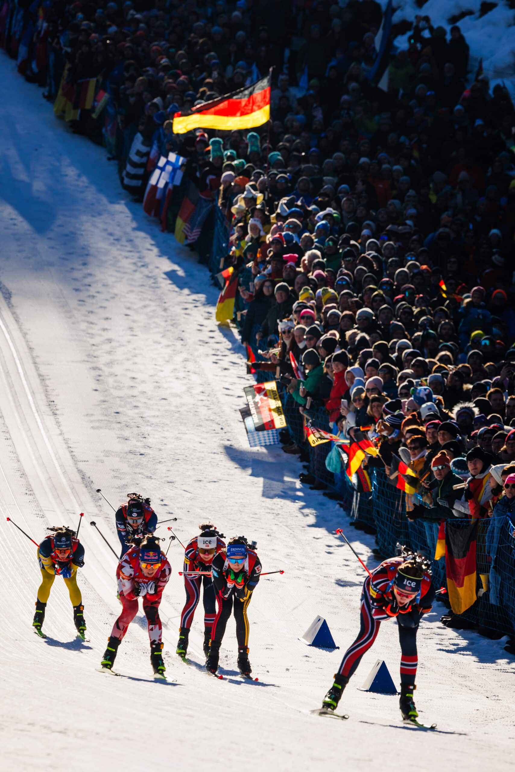 Biathletinnen im Rennen beim Weltcup in Ruhpolding, Zuschauer mit Fahnen säumen die Strecke.