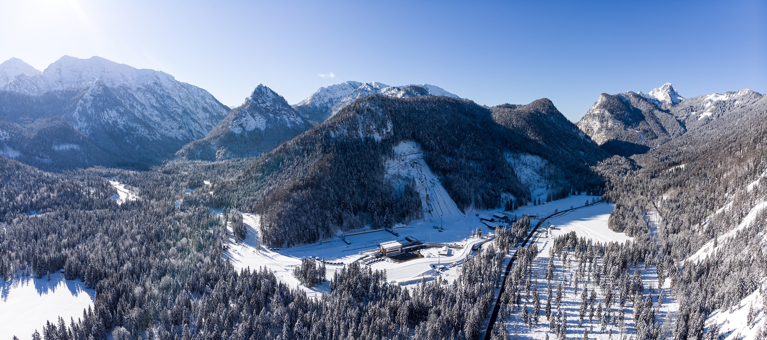 Winterliches Panorama der Chiemgau Arena inmitten verschneiter Berge und Wälder.