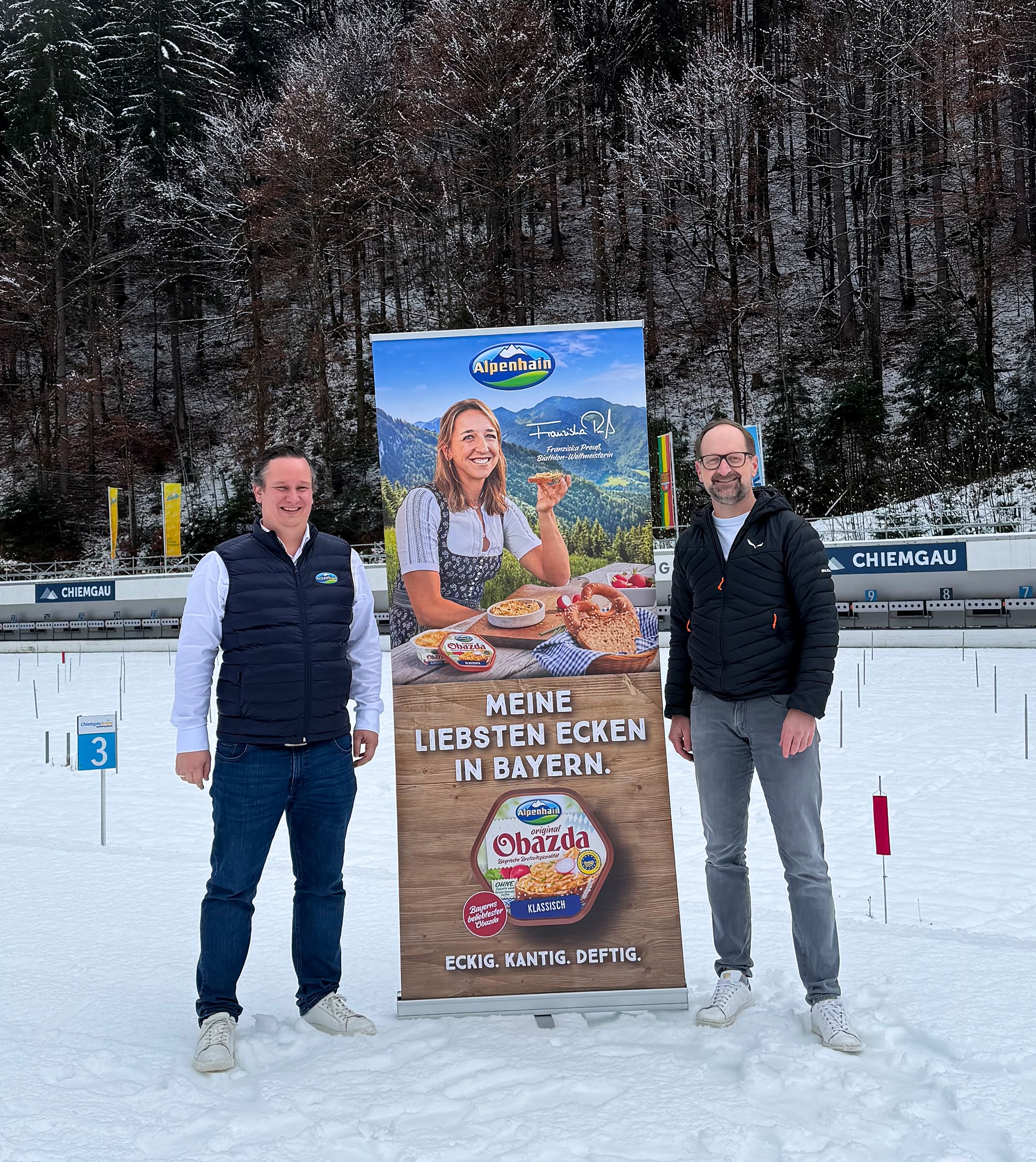 Vertreter von Alpenhain und der Chiemgau Arena vor Werbedisplay im Stadionbereich in Ruhpolding.