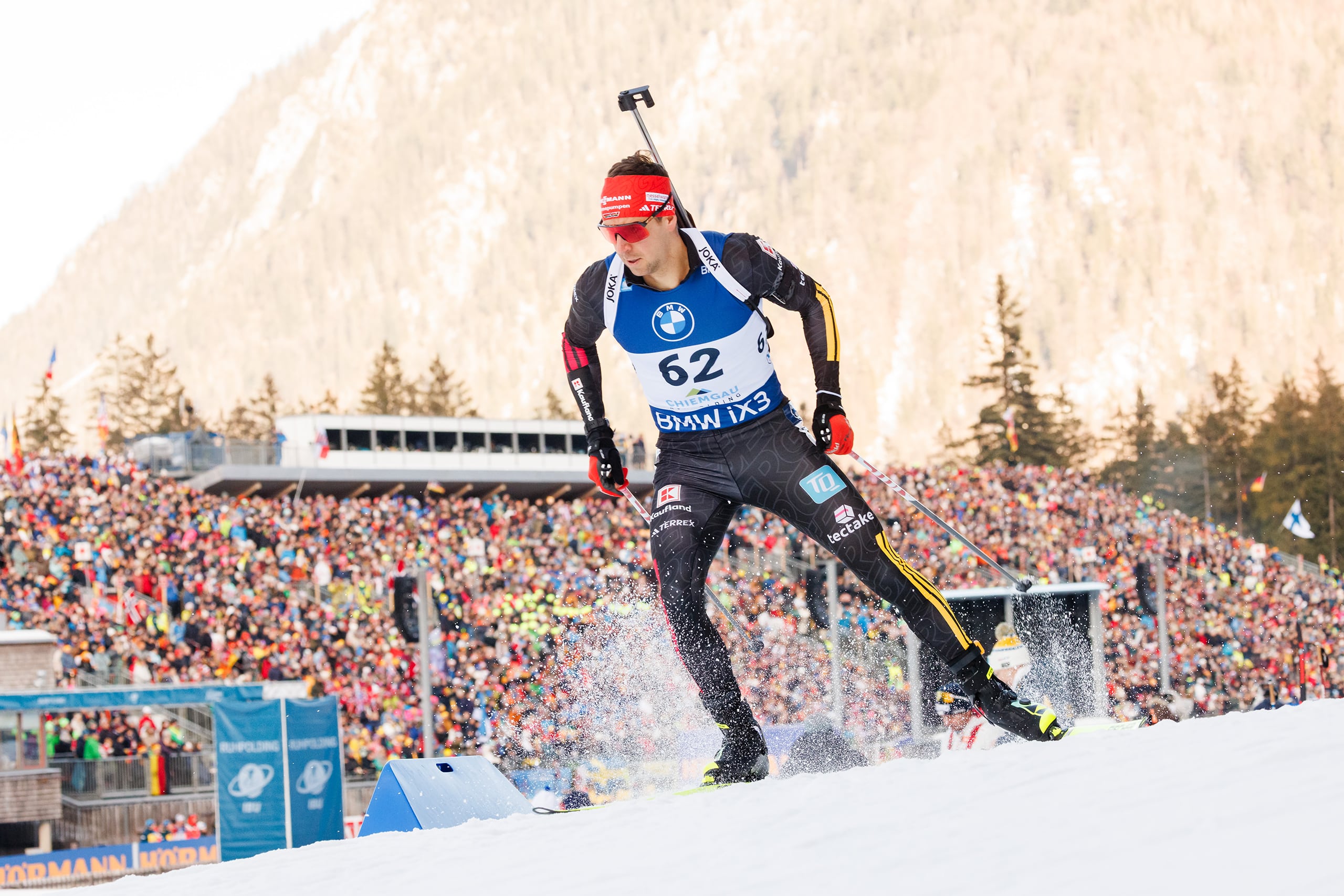Biathlet mit Startnummer 62 beim Weltcup in Ruhpolding vor dicht gefüllter Zuschauertribüne.