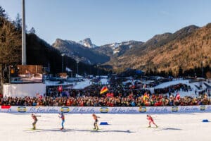 Biathlon-Wettkampf in der Chiemgau Arena mit voll besetzten Tribünen und Alpenpanorama im Hintergrund.
